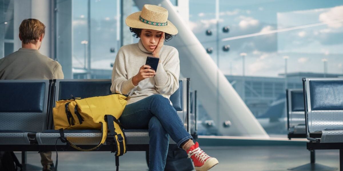 A woman sitting at an airport gate waiting for a delayed flight, relieved she bought travel insurance, one of the key steps on our international travel checklist
