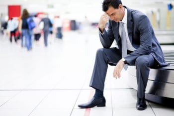 a suited man sitting at the airport without his luggage, wishing he had bought international personal property insurance