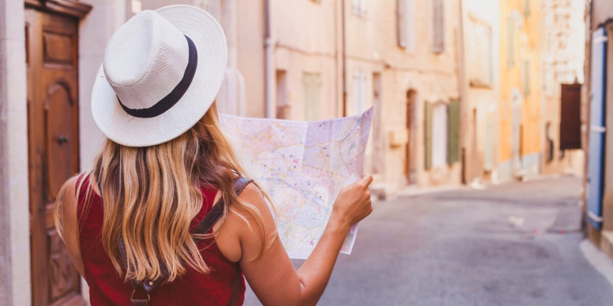 A woman walking down a street while holding a map, planning her next step, one of the key parts of how to plan an international trip.