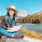 a female digital nomad working on a laptop against a mountain lake in autumn