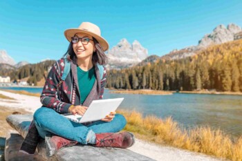 a female digital nomad working on a laptop against a mountain lake in autumn