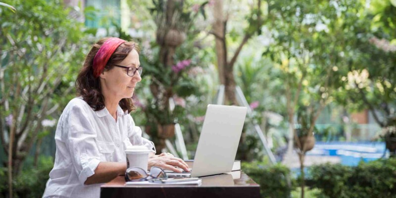 a female digital nomad working on her laptop in a tropical outdoor setting