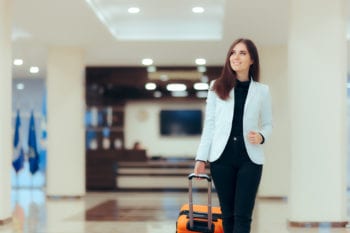 A woman pulls a suitcase through a hotel lobby, smiling about her choice to buy expat health insurance coverage abroad.