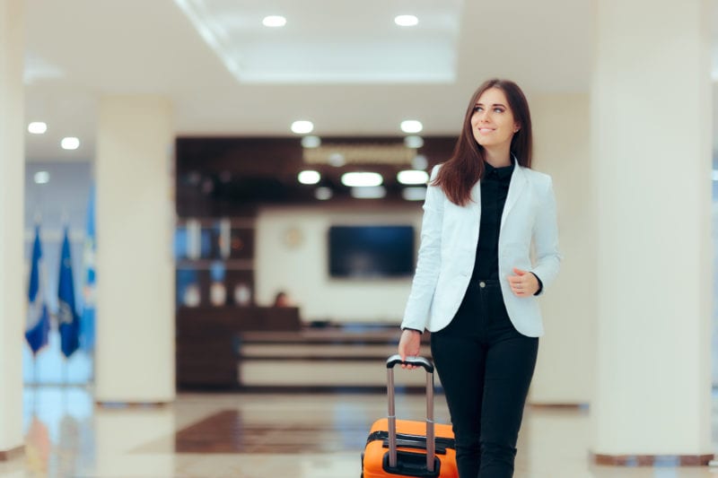 A woman pulls a suitcase through a hotel lobby, smiling about her choice to buy expat health insurance coverage abroad.