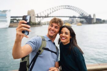 A happy couple taking a selfie in front of Sydney Harbour Bridge, having bought travel insurance for Australia