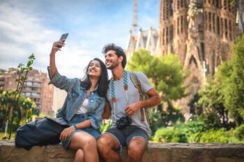 a happy couple taking a selfie in front of the Sagrada Familia in Barcelona, having purchased travel insurance for Spain