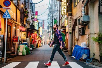 a male tourist crossing a street in a busy Japanese city, having purchased travel insurance for Japan