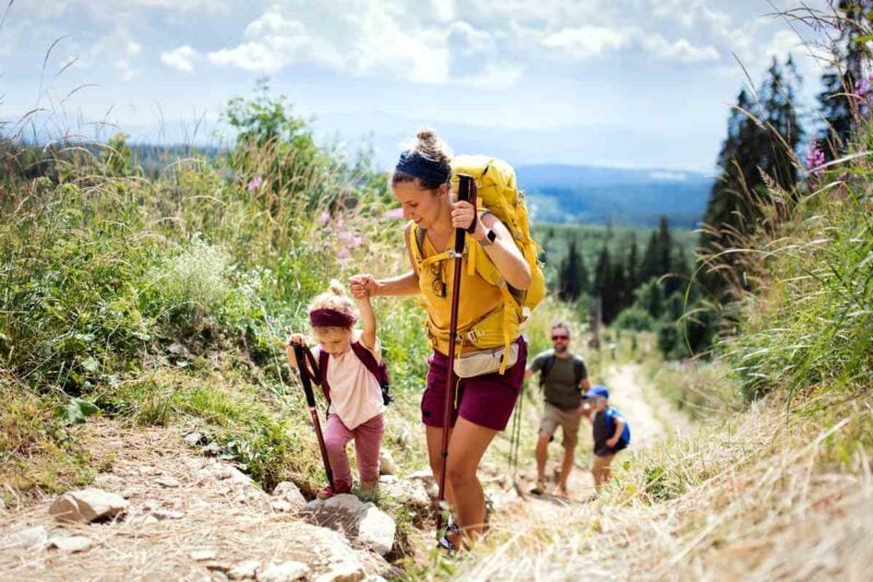 A husband and wife hiking with two young children happily talk about their decision to buy international health insurance.