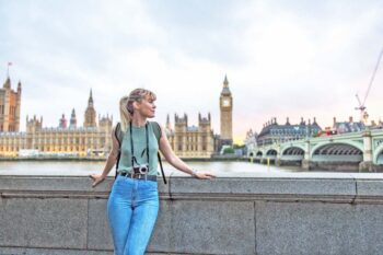 a young female tourist posing In front of the Palace of Westminster in London, having purchased UK travel insurance for her trip