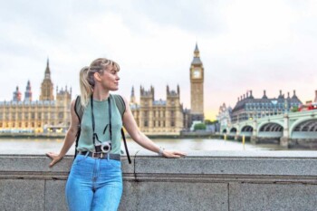 a young female tourist posing In front of the Palace of Westminster in London, having purchased UK travel insurance for her trip