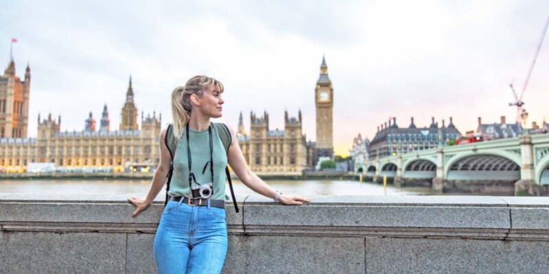 a young female tourist posing In front of the Palace of Westminster in London, having purchased UK travel insurance for her trip