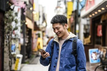 an asian man smiling at his cell phone as he makes a call abroad using our international calling codes