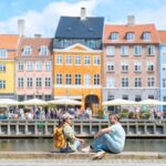 a happy couple sitting by the colorful waterfront buildings in Copenhagen, named among the most liveable cities in the world in 2025