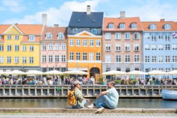 a happy couple sitting by the colorful waterfront buildings in Copenhagen, named among the most liveable cities in the world in 2025