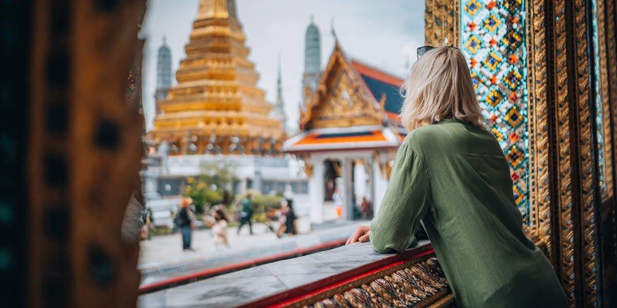 a woman looking out a window at the Grand Palace in Bangkok, where travel insurance for Thailand is advised