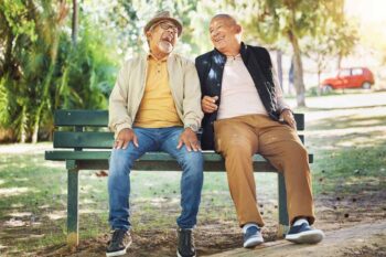 two elderly men sitting on a bench and laughing, indicating how life expectancy per country can differ