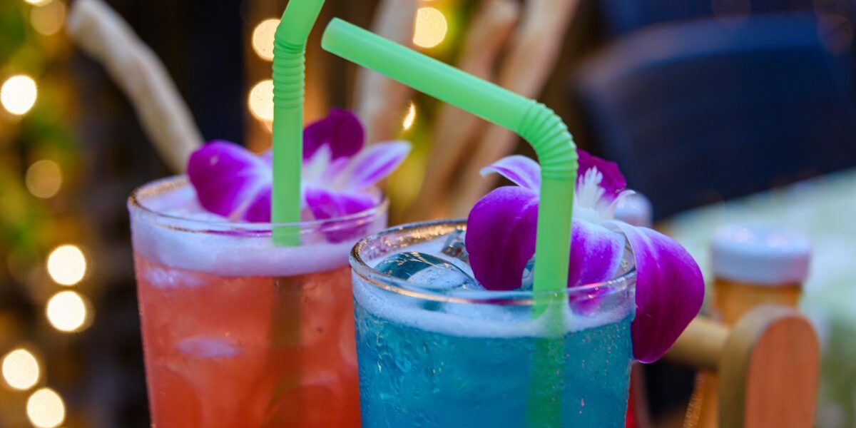 Red and blue cocktails with straws and purple flowers in a bar, indicating the need for travel insurance in Thailand in case of drink spiking