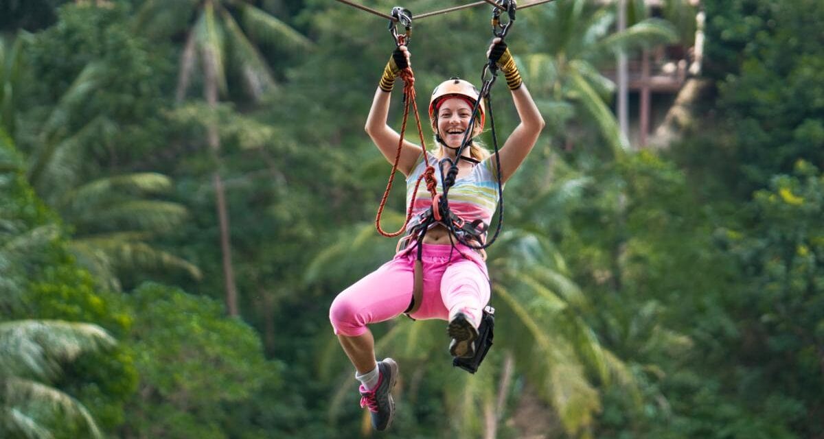 a woman ziplining in the rainforest, indicating the importance of having travel insurance for Thailand