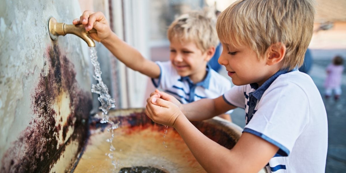 Little boys drinking tap water from a public sink in Italy, where it's advisable to buy travel insurance for Italy