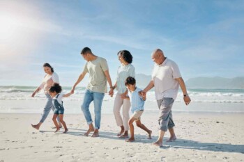 a multigenerational family holding hands and walking on a beach, indicating one of the biggest travel trends of 2025