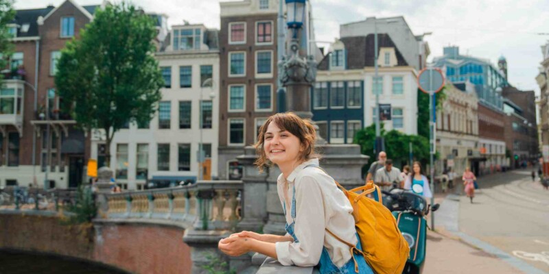 a happy female traveler standing on a bridge over a canal in Amsterdam, Netherlands