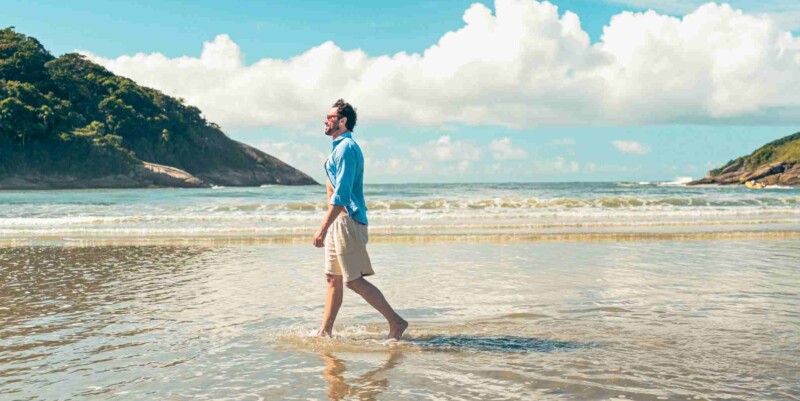 a man walking along a quiet beach in Brazil, having purchased travel insurance for Brazil before his trip