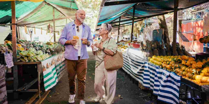 a senior couple walking through a food market in Brazil, having purchased travel insurance for Brazil before their trip