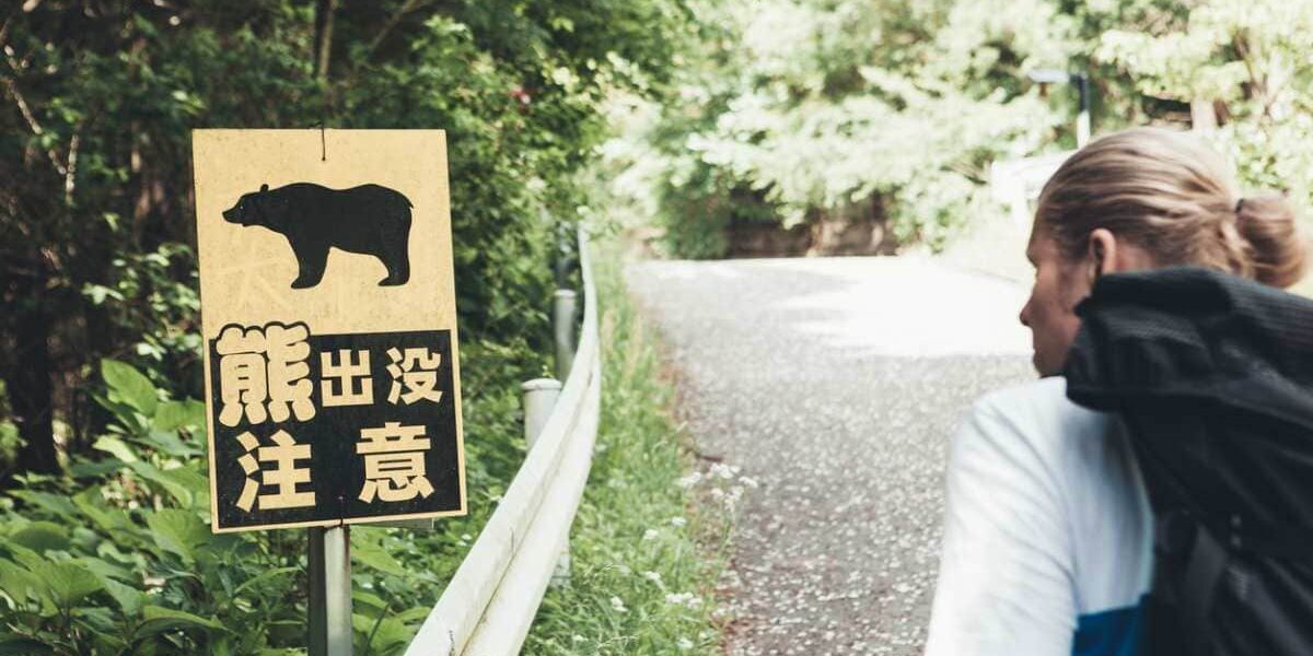 A tourist walking past a bear warning sign in a rural area of Japan, highlighting the important of buying robust travel insurance for Japan