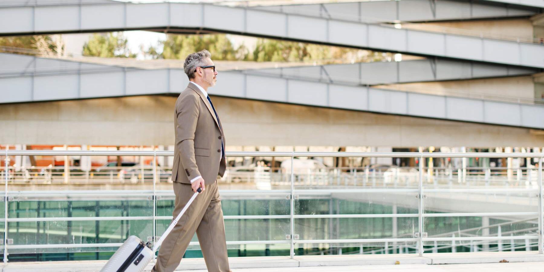 a seasoned businessman walking purposefully with a rolling suitcase in a clean, empty airport