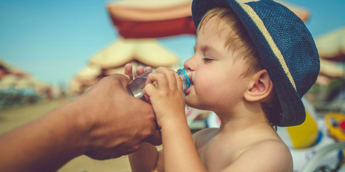 A child drinking water from a bottle on a beach during a hot day, illustrating the importance of staying hydrated and following safety tips, like buying travel insurance for Spain