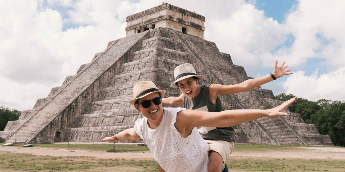 a happy couple posing in front of a pyramid in Mexico, where tourists are advised to buy travel insurance for Mexico