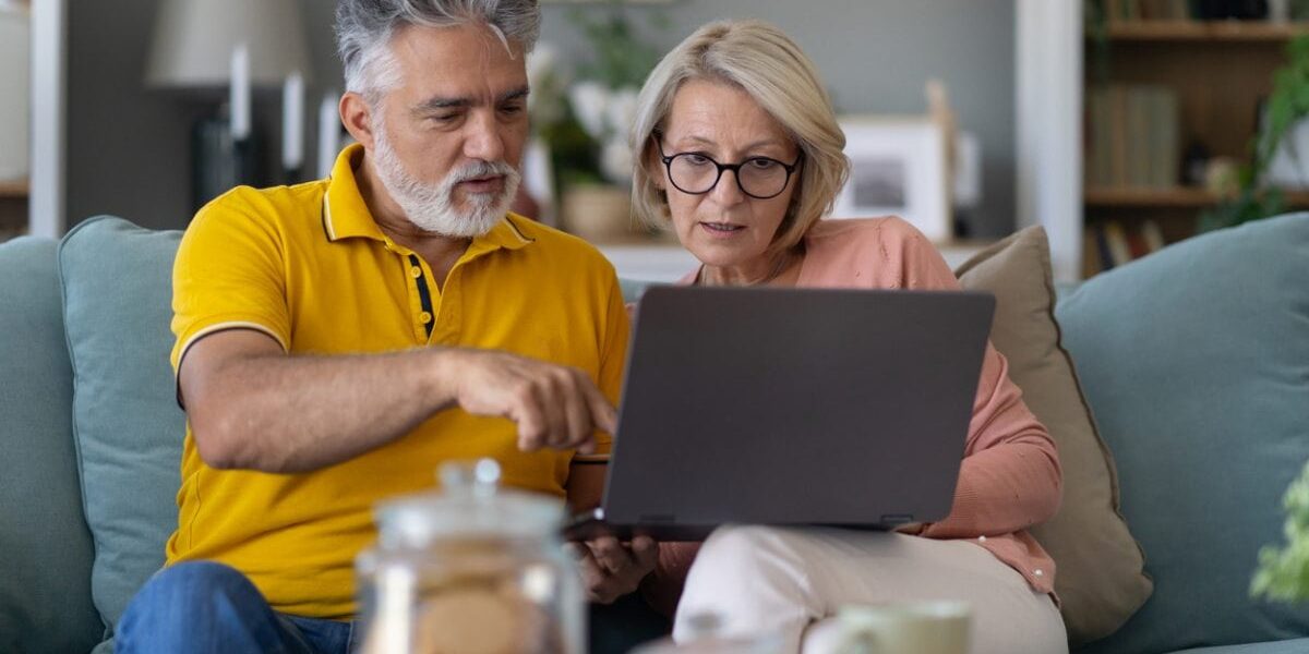 Senior couple sitting on a sofa using their laptop to compare international insurance plans