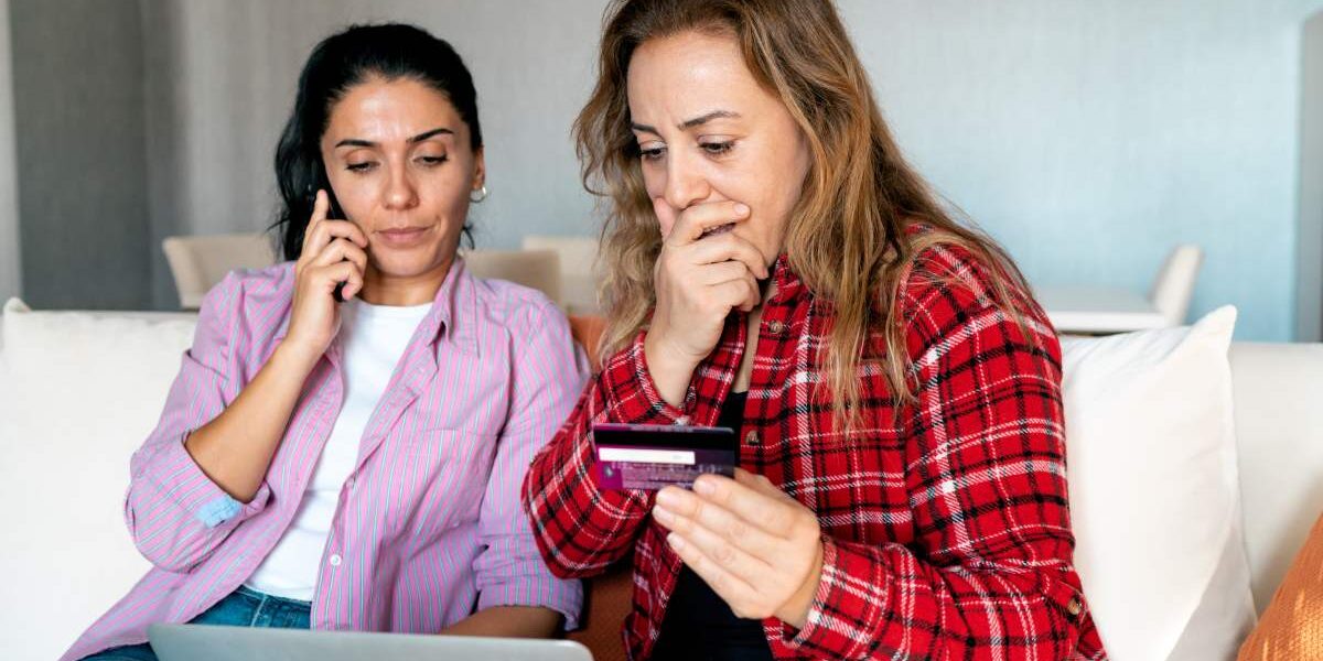 an upset woman holding her bank card as she realises she's fallen victim to one of the most common travel scams