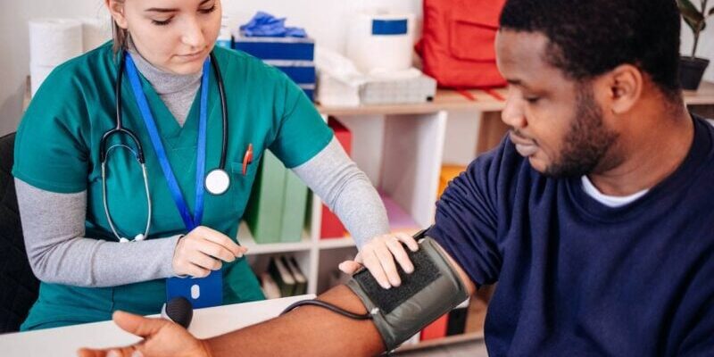 a medical assistant checking a young patient's blood pressure, indicating the importance of securing student group travel insurance for trip abroad and weighing up whether to buy travel insurance vs health insurance