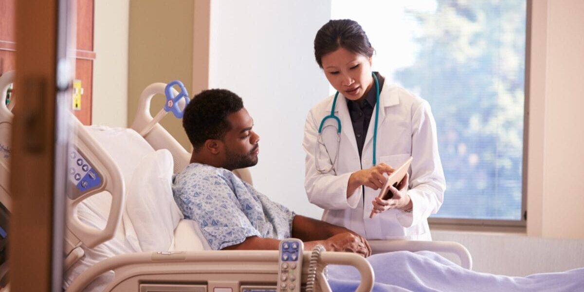 a male patient laying in a hospital bed talking to a female doctor, reflecting on the importance of having Schengen visa insurance when visiting Europe
