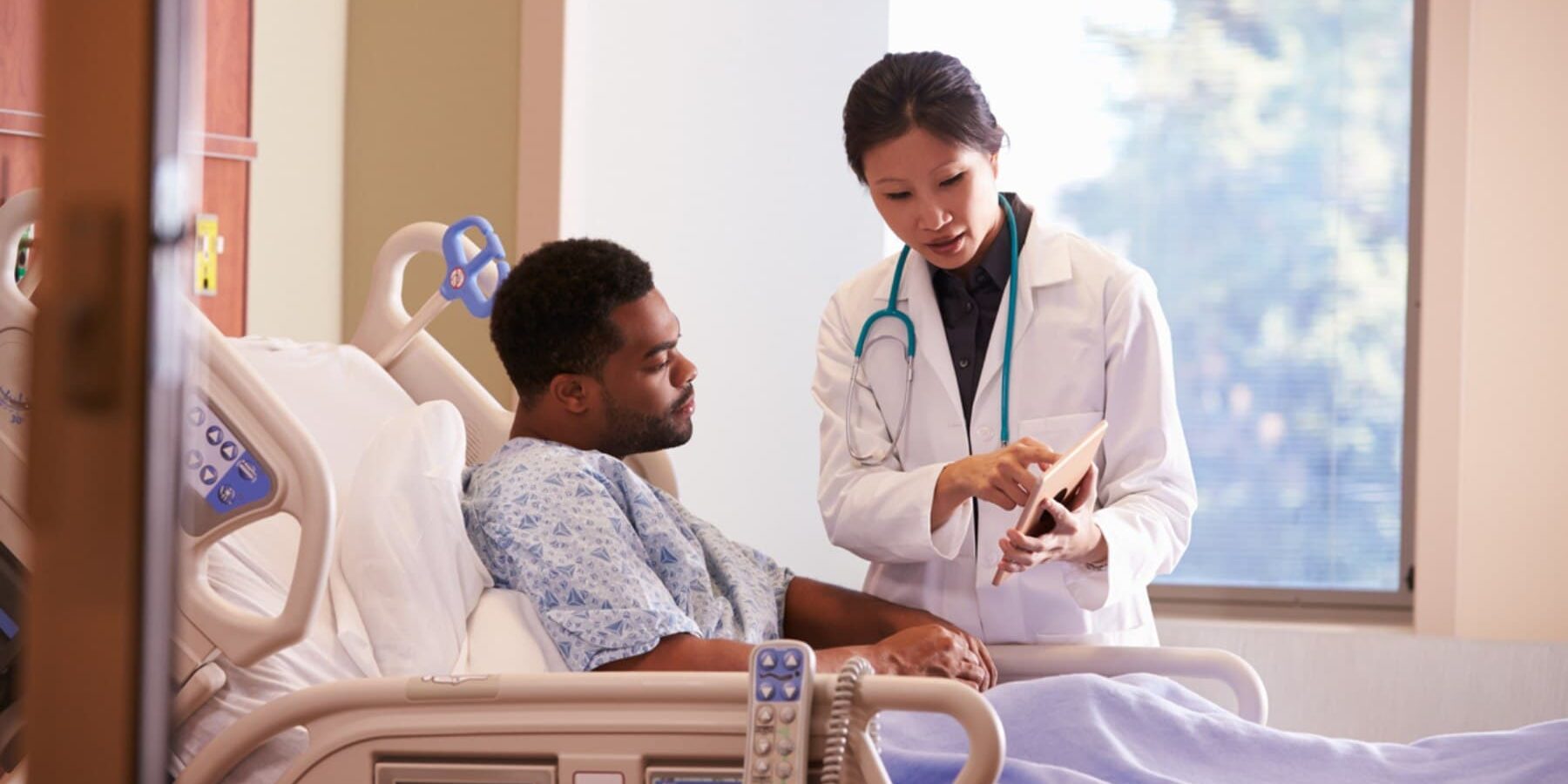 a male patient laying in a hospital bed talking to a female doctor, reflecting on the importance of having Schengen visa insurance when visiting Europe