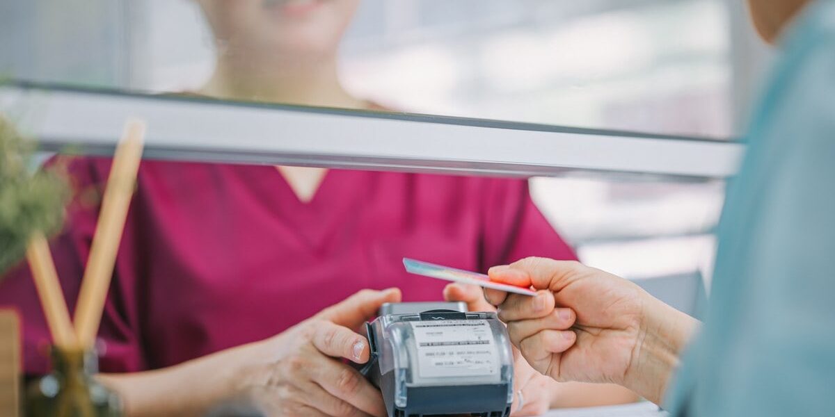 a woman paying a medical bill with a credit card, while a nurse holds the credit card reader in a hospital.