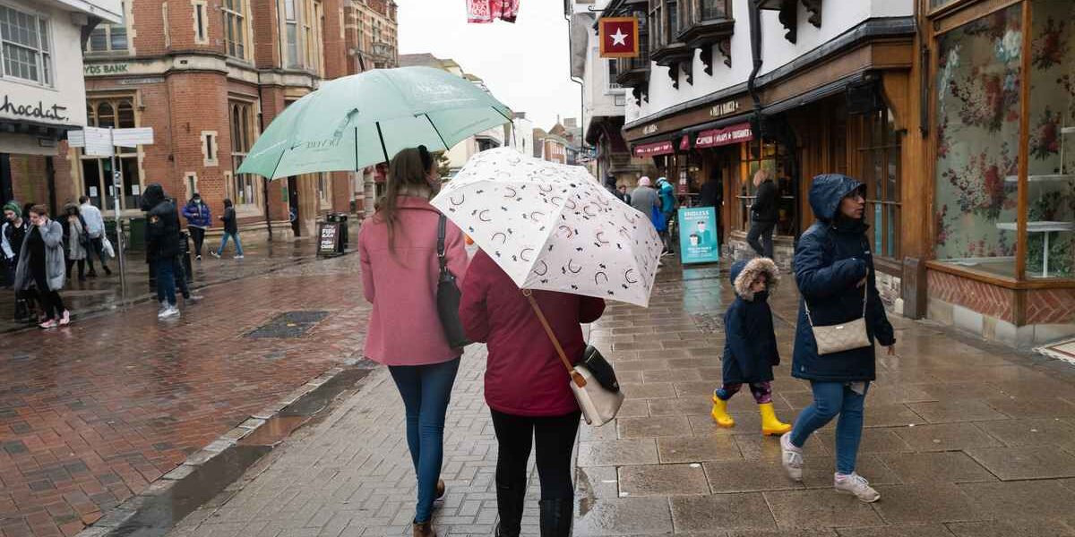 two shoppers walking along a UK high street with umbrellas on a rainy day